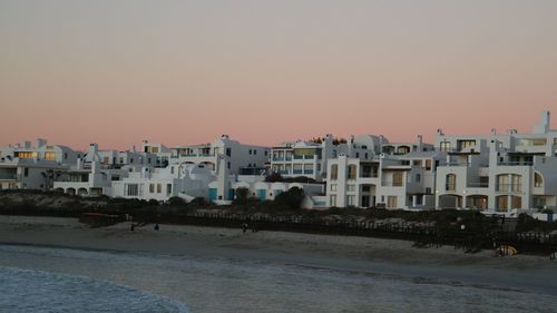 Buildings by sea against clear sky during sunset