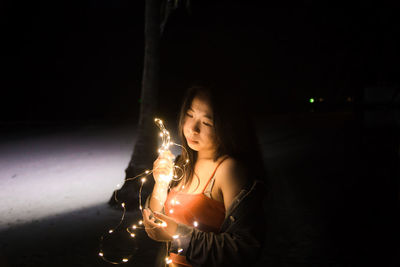 Young woman holding lit candle in the dark