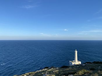 Lighthouse by sea against blue sky