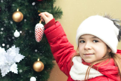 The girl hangs a christmas toy cone on the christmas tree. snowing.