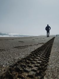 Rear view of man walking on beach against clear sky