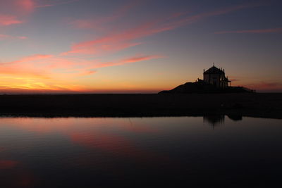 Silhouette lighthouse by sea against sky during sunset