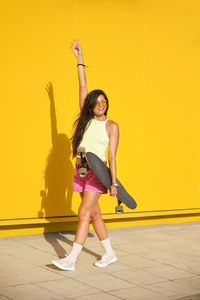 Full length portrait of a young woman standing against yellow wall