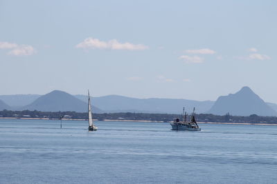 Boats in sea against cloudy sky