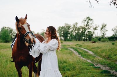 Young woman standing by horse on field