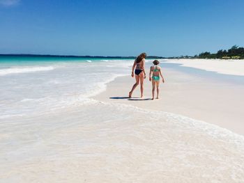 Full length of siblings walking at beach against sky