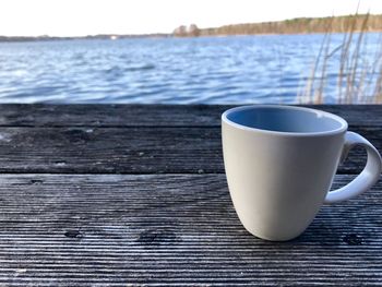 Coffee cup on table against lake