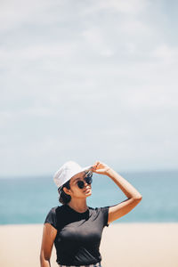 Woman wearing sunglasses while standing at beach against sky