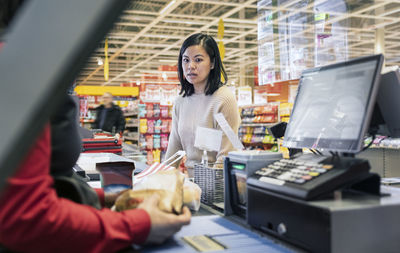 Young female customer talking to cashier at supermarket checkout