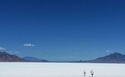 Rear view of man and woman walking at bonneville salt flats against sky