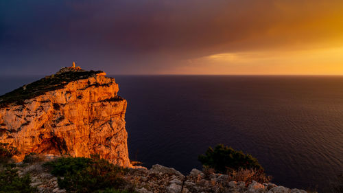 Rock formations by sea against sky during sunset