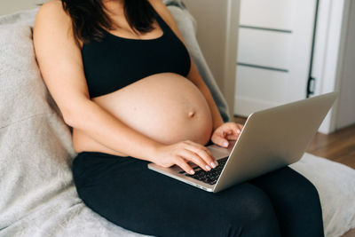 Unrecognizable pregnant business woman working at home on a laptop.