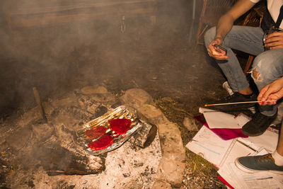 Low section of people sitting by food over fire on land at night