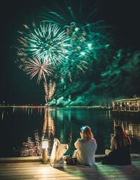 Rear view of people sitting by river at night