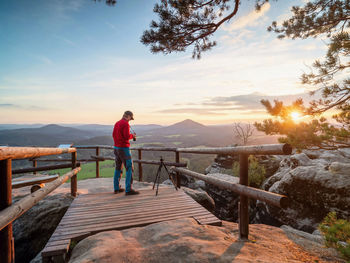 Man standing on railing against mountain during sunset