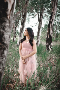 Woman standing by tree trunk in forest