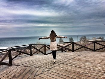 Rear view of woman standing on pier by sea against sky