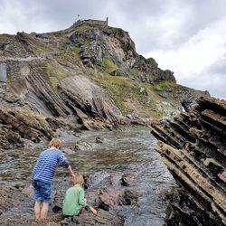 Rear view of people on rock by mountain against sky