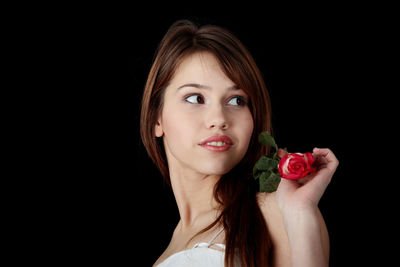 Portrait of woman holding rose against black background