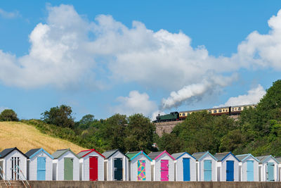 Colourful beach houses. row of  beach huts with steam train on stone viaduct against blue sky.