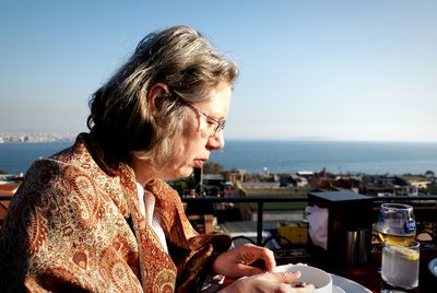 Side view of mature woman drinking coffee at cafe against sky