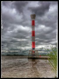 Lighthouse on sea against cloudy sky