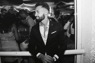 Young man looking away while standing against glass window