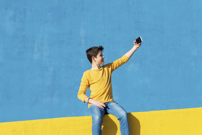 Young man photographing while standing on yellow wall