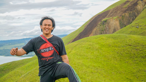 Portrait of smiling young woman standing on mountain against sky