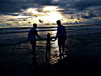 Father and son on beach against sky during sunset