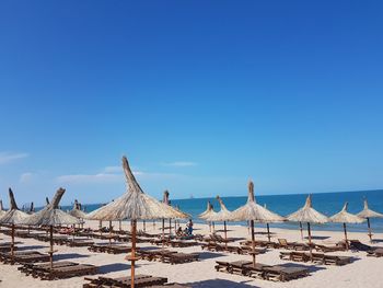 Chairs and thatched roofs at beach against blue sky