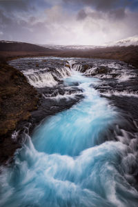 Scenic view of river flowing against cloudy sky