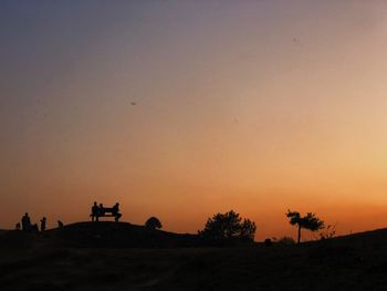 Silhouette people on land against sky during sunset