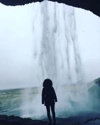 Rear view of woman looking waterfall while standing in cave