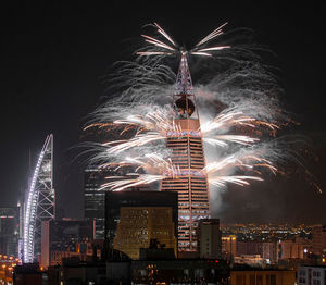 Firework display in city against sky at night