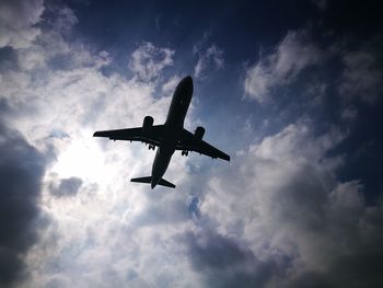 Low angle view of silhouette airplane flying against cloudy sky