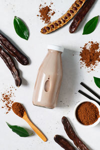 Carob drinks in bottle and carob beans, powder on white background, top view, vertical