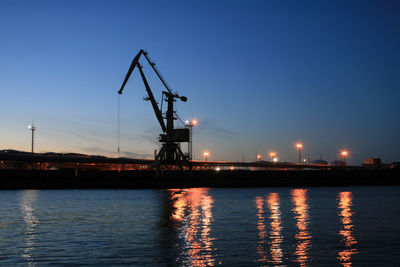 Cranes at commercial dock against sky at dusk