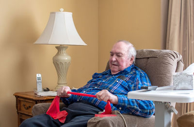 Senior male uses a resistance exercise band to exercise at home in his lift chair