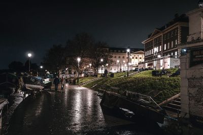 Illuminated street amidst buildings against sky during rainy season