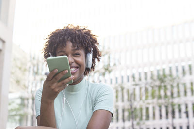 Young curly woman recording an audio message through her smartphone