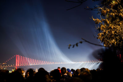 People against illuminated bridge in city at night