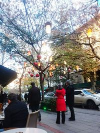 People by illuminated tree in city against sky