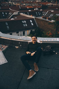 High angle full length of happy young man relaxing on illuminated terrace during party at dusk