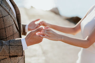 Midsection of bride and groom holding hands while standing outdoors