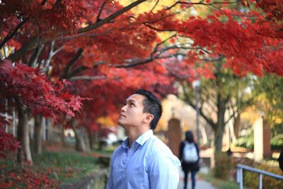 Portrait of smiling young woman standing by trees during autumn