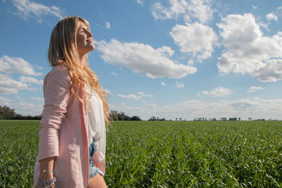 Young woman standing on field against sky