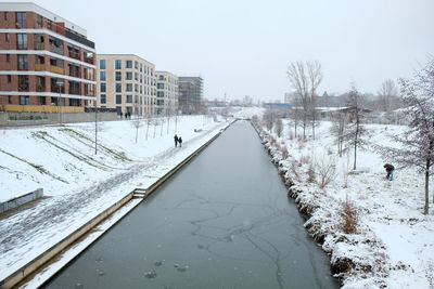 Snow covered road by canal against clear sky