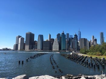 Sea in front of cityscape against clear blue sky