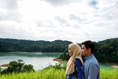 Couple standing by lake against sky